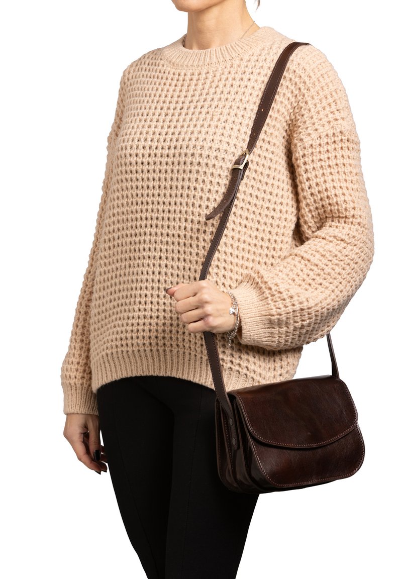 Borsa a tracolla in pelle marrone con pattina, cuciture a contrasto e una lunga tracolla regolabile, abbinata a un maglione beige texturizzato e pantaloni neri.