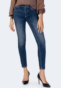 Tunna blå jeans i denim, med en medelhög midja, subtila slitageeffekter och en figurnära silhuett. I kombination med svarta stilettklackar.