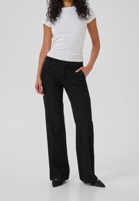 Mustat farkku-laahus-housut, joissa on etutaskut, yhdistettynä istuvaan valkoiseen lyhythihaiseen paitaan, jossa on pieni emblem rintamuksessa.