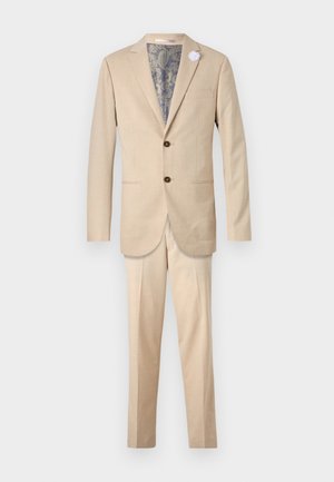 Beige Anzug bestehend aus einem einreihigen Sakko mit braunen Knöpfen und einer Hose, die ein Innenfutter mit Paisleymuster aufweist.