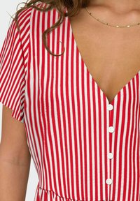 Robe rayée rouge et blanche à manches courtes avec un col en V et cinq boutons blancs sur le devant, présentant un tissu texturé.