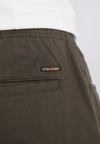 Oliwkowe bawełniane szorty z tylną kieszenią oraz naszywką logo Volcom w czerni i pomarańczu. Gładka tekstura i prosty krój.