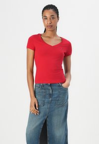 T-shirt rouge ajusté à manches courtes et col en V, associé à une jupe maxi en denim bleu avec une fente à l'avant et des poches.