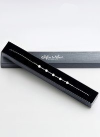 Silverarmband med sfäriska vita pärlor, arrangerade längs en delikat kedja, presenterad i en svart sammetklädd box.