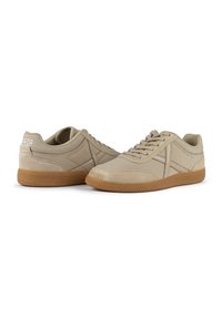 Zapatillas beige con cordones, con una parte superior de tejido suave, puntera reforzada y suela de goma. Presentan un logo discreto en el talón.