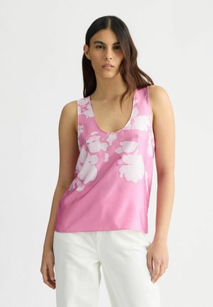 Ärmellose rosa Bluse mit floralem Muster, aus glattem Stoff gefertigt. Sie hat einen runden Ausschnitt und eine fließende Passform, kombiniert mit weißen Hosen.