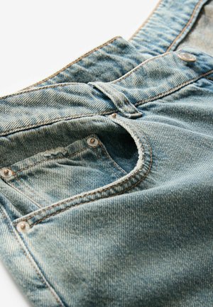 Heledadsin sinised teksad, millel on tekstureeritud pind, eestasku, nööbikipit ja kontrastset oranži õmblust. 