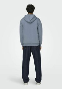 Lichtblauwe hoodie met een trekkoord in de capuchon, gecombineerd met loszittende donkerblauwe spijkerbroek. Glad materiaal, relaxte pasvorm.