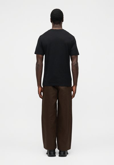 Čierne bavlnené tričko s krátkym rukávom, skombinované so širokými hnedými nohavicami. Oblečenie je doplnené čiernou obuvou.