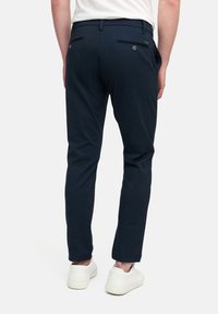 Navy blauwe broek met een slim fit, met achterzakken met knopsluitingen en een soepele stoftextuur. Gedragen met witte sneakers.