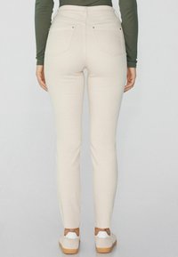 Jeans skinny beiges hechos de una tela suave, con una cintura de media altura, dos bolsillos traseros y una textura lisa. Combinados con calzado claro.