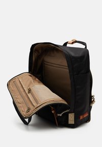 Black backpack with a tan interior, featuring a zippered compartment, mesh pocket, and leather accents. Opened to reveal spacious storage.