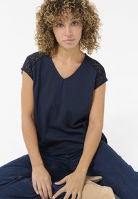 Haut bleu marine à manches courtes avec un décolleté en V et des accents en dentelle sur les épaules. Tissu en coton doux avec une coupe décontractée.