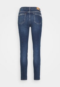 Skinny jeans in dark blue denim. Features a smooth texture, two back pockets, and a leather tag at the waist. Fitted fit.
