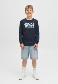 Cămașă cu mânecă lungă de marine cu "JACK & JONES" imprimat în litere colorate, asortată cu pantaloni scurți din denim deschis și adidași albi.