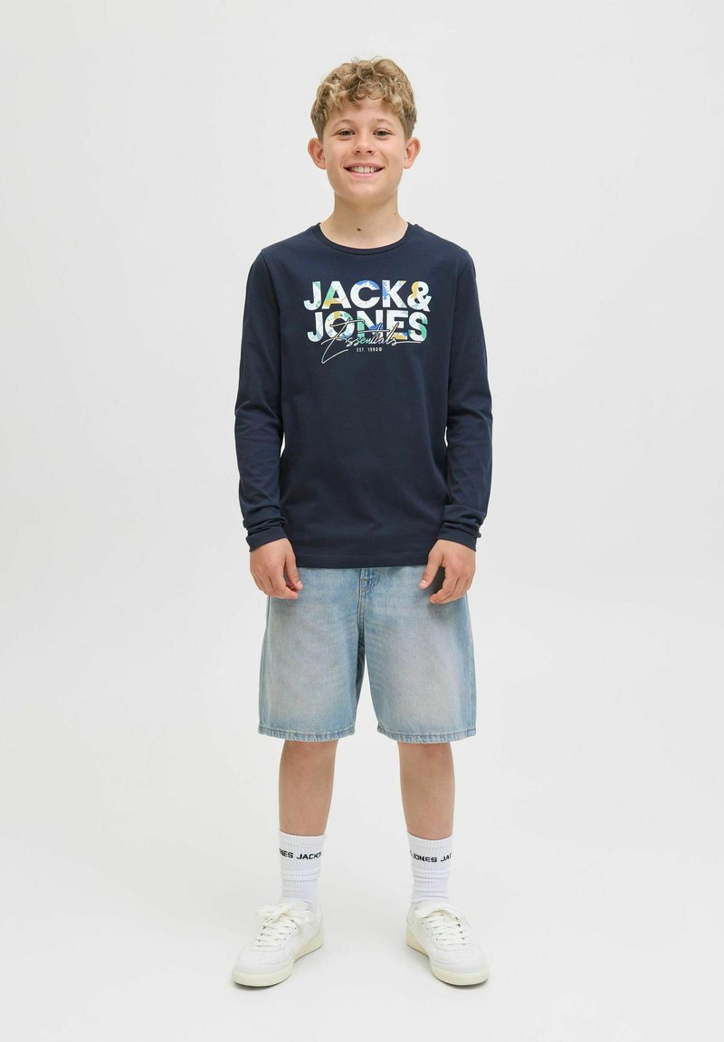 Cămașă cu mânecă lungă de marine cu "JACK & JONES" imprimat în litere colorate, asortată cu pantaloni scurți din denim deschis și adidași albi.