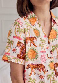 Collared short-sleeve shirt with colorful tiger, palm tree, sun, and star patterns on white fabric worn by a person with short brown hair.