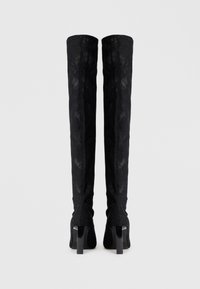 Botas de encaje negro por encima de la rodilla con un acabado texturizado, que presentan un borde superior curvado y tacones altos en bloque.