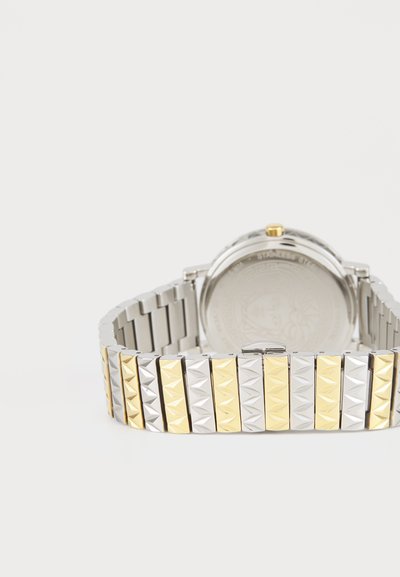 Montre argentée et dorée avec un bracelet métallique présentant des motifs en losange en relief. Boîtier rond avec une finition métallique et couronne ronde.