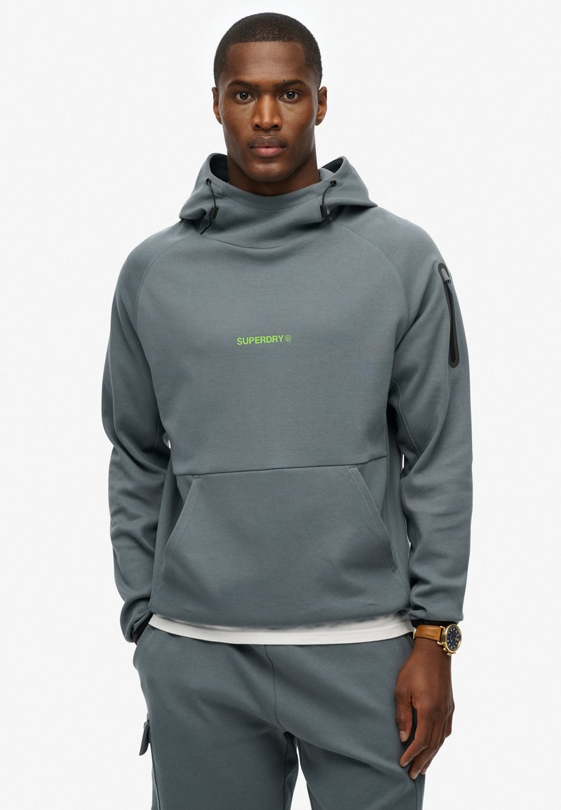 Sudadera gris con bolsillo canguro en la parte frontal, cremallera lateral y logo verde. Fabricada en un tejido suave con un ajuste cómodo y relajado.