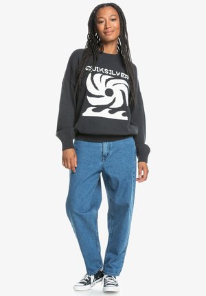 Sweatshirt noir avec un graphique de vague en spirale blanche, associé à un jean baggy bleu clair et des baskets noir et blanc. Coupe décontractée et poignets côtelés.