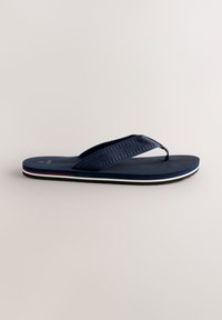 Dunkelblaue Flip-Flops aus strukturiertem Gummi, mit einem gewebten Riemen, einer flachen Sohle und einem weißen sowie roten Akzentstreifen entlang des Randes.