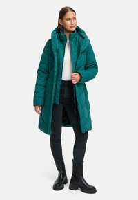 Teal puffer coat with a hood, featuring a quilted design, long sleeves, and a zip closure, paired with black jeans and chunky black boots.