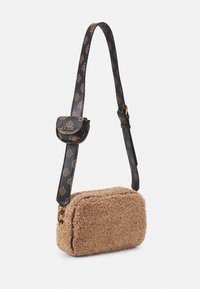 Hnědá kabelka přes rameno s podšívkou shearling a černým vzorovaným popruhem. Má malý přední klopový díl se zlatým logem a zipové uzavírání hlavní přihrádky.