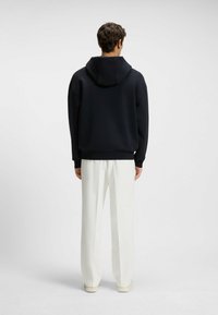 Felpa blu navy con vestibilità rilassata, dotata di cappuccio e polsini a coste. Abbinata a pantaloni bianchi a gamba larga e scarpe chiare.