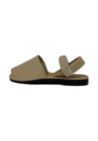 Sandal in pelle beige con suola piatta, design aperto e cinturino alla caviglia regolabile. Presenta cuciture a contrasto lungo i bordi.