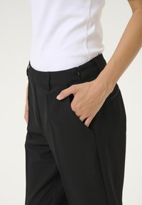 Pantaloni neri con vita aderente, tasche laterali e una texture di tessuto liscia. Presentano una chiusura con zip e un design su misura.