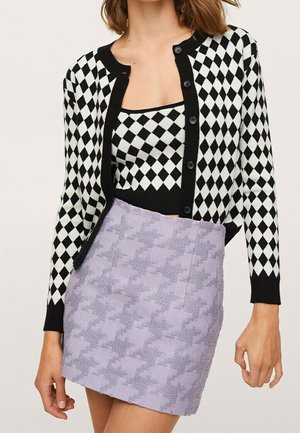 Mujer con cárdigan y top con patrón de rombos en blanco y negro y minifalda lavanda texturizada.