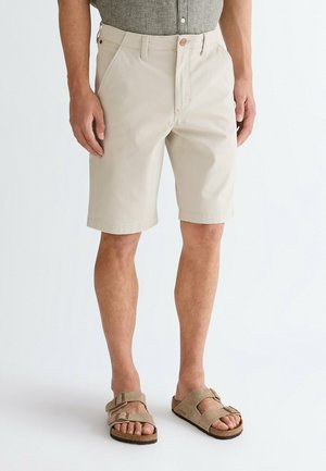 Beige shorts lavet af letvægtsstof, lige skåret med forlommer og knaplukning. Bruges med brune sandaler med justerbare stropper.
