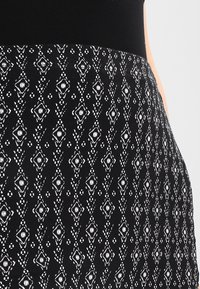 Jupe en tissu noir avec un motif géométrique en losanges blancs agrémenté de fleurs, texture lisse et taille ajustée.