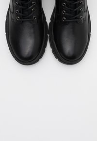 Bottines en cuir noir à bout rond, avec six œillets et semelles en caoutchouc épaisses. Surface lisse avec une finition élégante.
