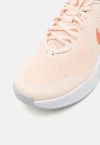 Lys ferskenfarvet mesh sportssko med struktureret overflade, hvid mellemsål, reflekterende detaljer og kontrasterende orange swoosh-logo.