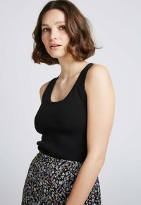 Débardeur noir côtelé avec un large col en cœur, associé à une jupe à motifs floraux avec des fleurs bleues et jaunes sur un fond noir.