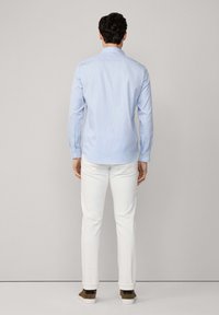 Camisa abotonada a rayas azul claro con mangas largas, metida dentro de pantalones blancos, combinada con zapatillas marrones y blancas.