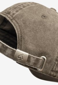 Brązowa tkaninowa czapka o teksturowanej powierzchni, z metalowym zapięciem z detalem logo na regulowanym pasku. Zaokrąglony kształt daszka.