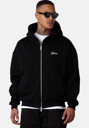 Haut de hoodie noir zippé avec une capuche structurée, des poignets à côtes et un ourlet. Présente un logo brodé sur la poitrine, fabriqué en tissu doux.