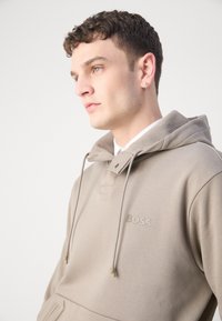 Hooded beige sweatshirt with a textured finish, featuring a front pocket and embroidered "BOSS" logo in a matching color.