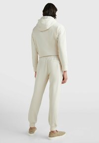 Conjunto de sudadera beige y pantalones de chándal de tejido suave. Con capucha, puños acanalados y detalles en los bolsillos laterales. Combinado con unos zapatos de tela beige claro.