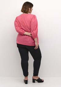 Blusa rosa a maniche a sbuffo con motivo testurizzato, abbinata a jeans skinny neri e mule neri con tacco blocco. Vista da dietro.