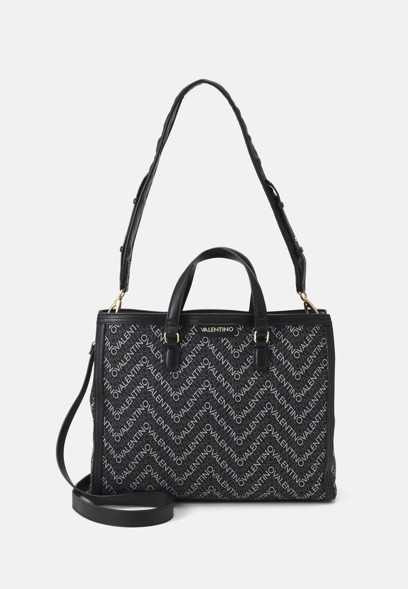 Black tote bag with a logo pattern, featuring double handles and a detachable shoulder strap. Gold hardware accents enhance the design.