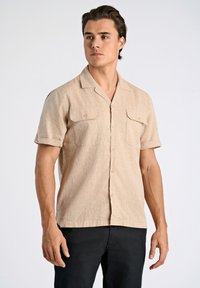 Korte mouwen, knopjeshemd in lichtbeige, met twee borstzakken en een subtiele textuur. Opgerolde mouwen en een ontspannen pasvorm.