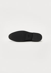 Black shoe sole with a smooth texture, rounded toe, slight heel, and embossed branding. Sturdy rubber material with traction pattern.