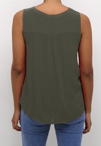 Haut sans manches vert olive avec un col rond, un léger plissage à l'arrière et un ourlet arrondi. Associé à un jean bleu ajusté.