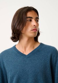 V-Ausschnitt-Pullover in einem tiefblauen Farbton, aus weichem, strukturiertem Stoff gefertigt. Das Design verfügt über einen gerippten Kragen und eine lockere Passform, die das Dekolleté zur Geltung bringt.