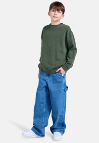 Groene sweatshirt met een ronde hals en geribde manchetten, gecombineerd met oversized blauwe spijkerbroek en witte sneakers.