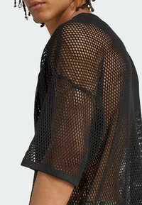 Black mesh shirt featuring oversized fit, short sleeves, and a loose, open-knit design. Ribbed neckline and hem details are visible.